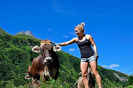 Volunteering Tirol: Sophie unterbricht die Schwendarbeit, um die neugierigen Kühe zu streicheln. Waxeggalm im Zemmgrund, Hochgebirgsnaturpark Zillertaler Alpen, Tirol, Österreich