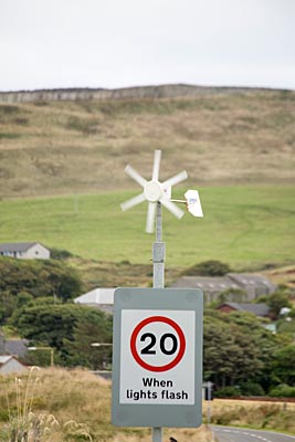 Schottland - Orkney Inseln - Windrad auf einem Verkehrsschild "Höchstgeschwindigkeit 20 Meilen/Stunde" erzeugt den Strom zum Betrieb der Warnblinker
